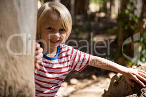 Happy little girl leaning on the tree trunk on a sunny day