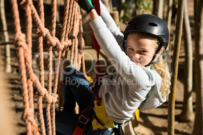 Little girl wearing helmet climbing on rope fence