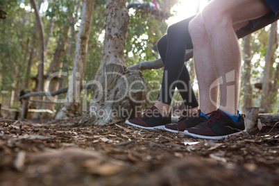 Legs of man and woman sitting on log of wood in the forest