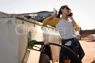 Woman talking on mobile phone while filling petrol in car