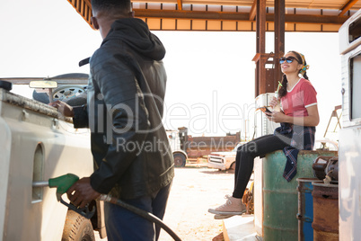 Man filling petrol in car while woman sitting at petrol pump station
