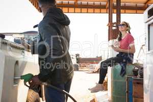 Man filling petrol in car while woman sitting at petrol pump station