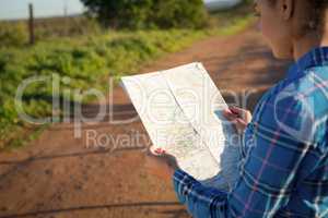 Woman holding a map standing on dirt track on a sunny day