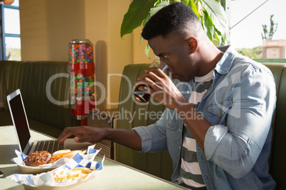 Young man having cold drink while using laptop