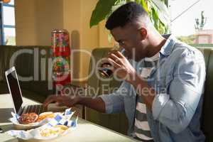 Young man having cold drink while using laptop