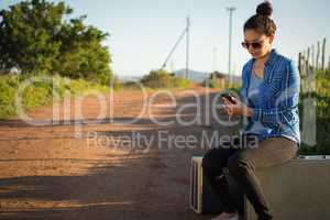 Woman using her mobile phone while sitting on suitcase