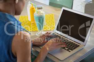 Woman using laptop while having milkshake in the restaurant