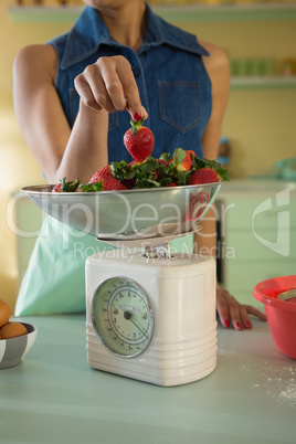 Young woman weighing strawberries on weighing machine in the kitchen