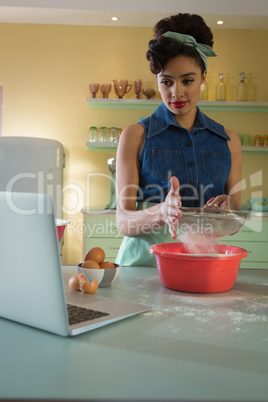 Woman straining flour while using laptop