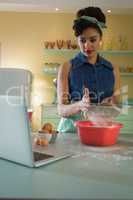 Woman straining flour while using laptop