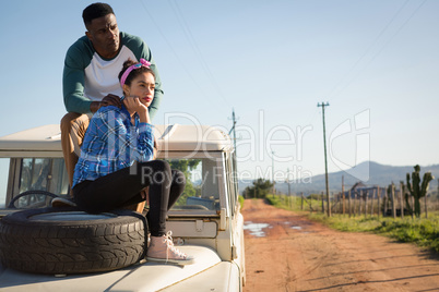 Couple sitting on car bonnet at countryside