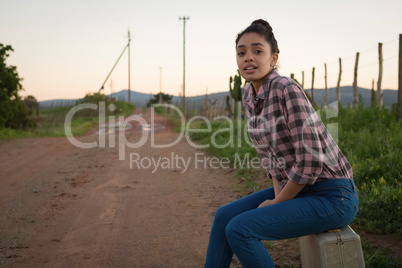 Woman sitting on suitcase at countryside
