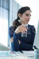 Thoughtful female executive holding glass of water at desk