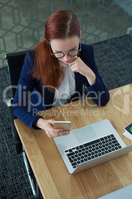 High angle view of female executive using mobile phone at desk