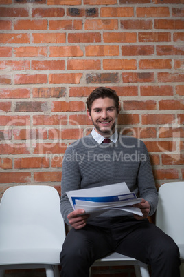 Male executive sitting with documents in waiting area