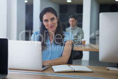 Smiling female executive working on laptop at desk Smiling female executive working on laptop at desk