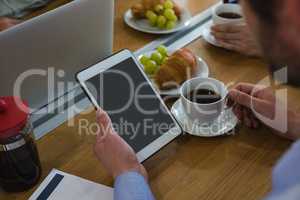 Male executive having coffee while using tablet