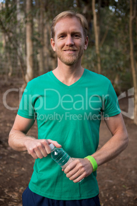 Smiling young man standing in the forest and holding water bottle in his hands