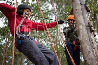 Young man wearing safety helmet crossing zip line while woman looking at him