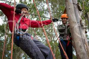 Young man wearing safety helmet crossing zip line while woman looking at him