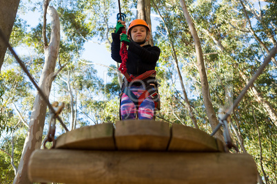 Little girl wearing helmet holding rope and standing on wooden platform