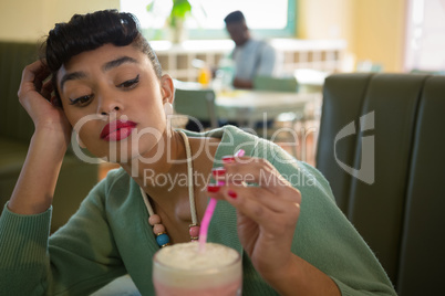 Woman keeping her head on hand while looking at milkshake