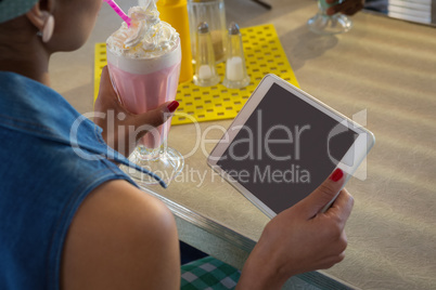 Woman using tablet while having milkshake in the restaurant