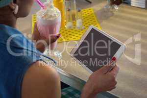 Woman using tablet while having milkshake in the restaurant