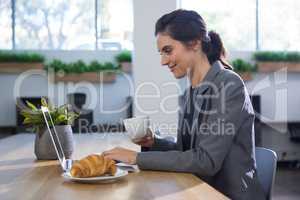 Female executive working at desk while having coffee at table