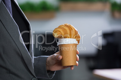 Mid section of female executive holding coffee and croissant