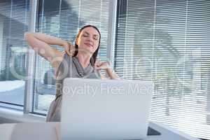 Tired female executive stretching her arms at desk