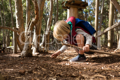 Little girl with backpack holding stick in her hand playing with rock