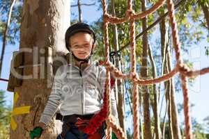 Little girl wearing helmet standing near rope fence