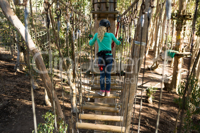 Little girl wearing helmet crossing wooden bridge in the forest