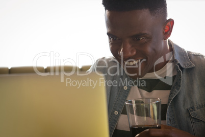 Happy young man holding glass while working on laptop