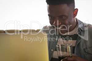 Happy young man holding glass while working on laptop