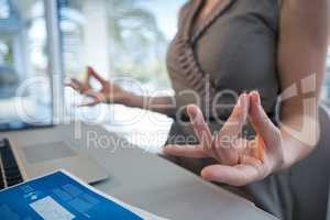 Mid section of female executive performing yoga at desk