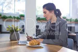 Female executive working at desk while having breakfast