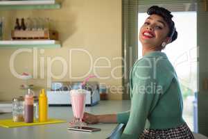 Smiling woman holding milkshake glass looking into camera at restaurant