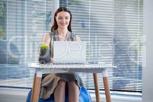 Female executive sitting on exercise ball while using laptop at desk