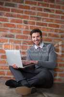 Smiling executive using laptop against brick wall