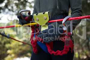 Woman adjusting her harness on zip line cable in the forest on a sunny day