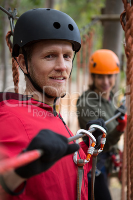Smiling young man wearing safety helmet holding zip line cable in the forest