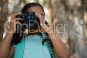 Little girl with backpack taking photos from dslr camera in the forest