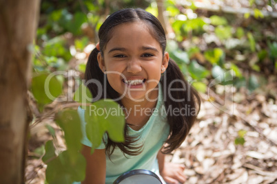 Happy little girl holding magnifying glass in the forest