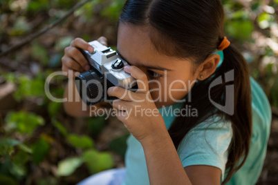 Little girl with backpack taking photo with camera on a sunny day in the forest