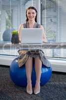Female executive sitting on exercise ball while working at desk