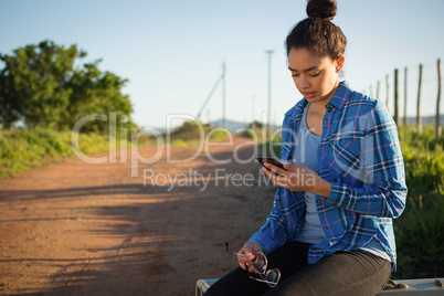 Woman using her mobile phone while sitting on suitcase