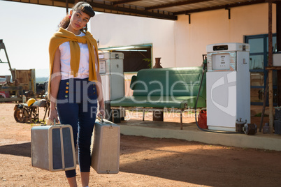 Woman standing with suitcase at petrol pump station
