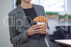 Mid section of female executive holding coffee and croissant